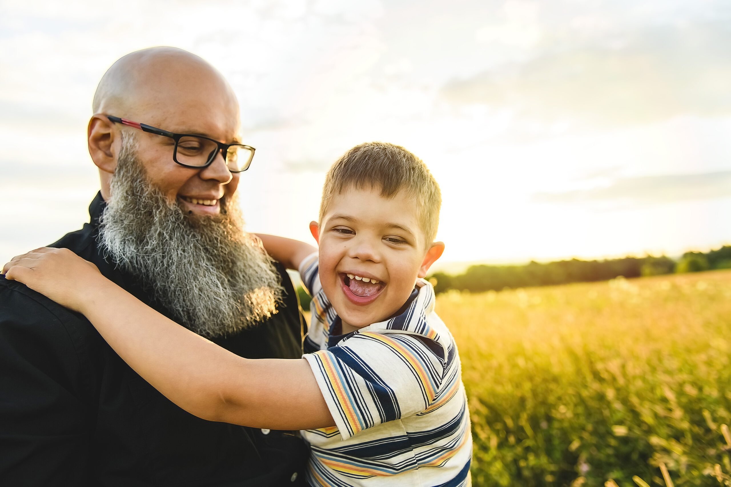 Portrait of a little boy with down syndrome in sunset on summer season with his father
